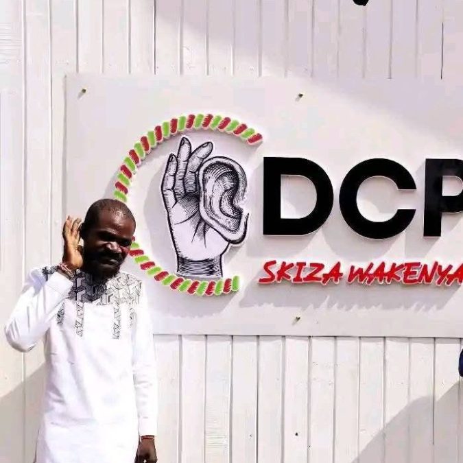 Raila's diehard supporter Nuru Okanga posing next to Gachagua's DCP Party signboard. PHOTO/https://www.facebook.com/profile.php?id=100084859213350