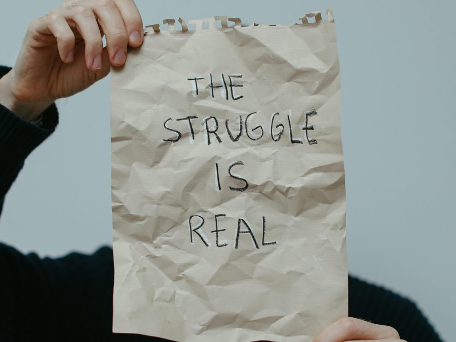 Man holding a creased paper sheet in front of him with a sign the struggle is real