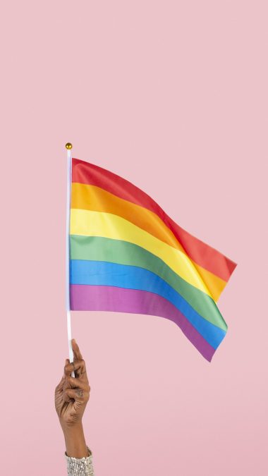 The pride flag flutters in the wind as a person proudly hoists it, celebrating LGBTQ+ visibility. PHOTO/Pexels