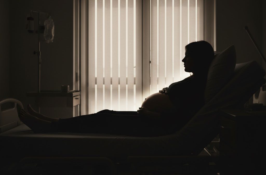 A silhouette of a pregnant woman lying on a hospital bed. Image is used for illustration.
