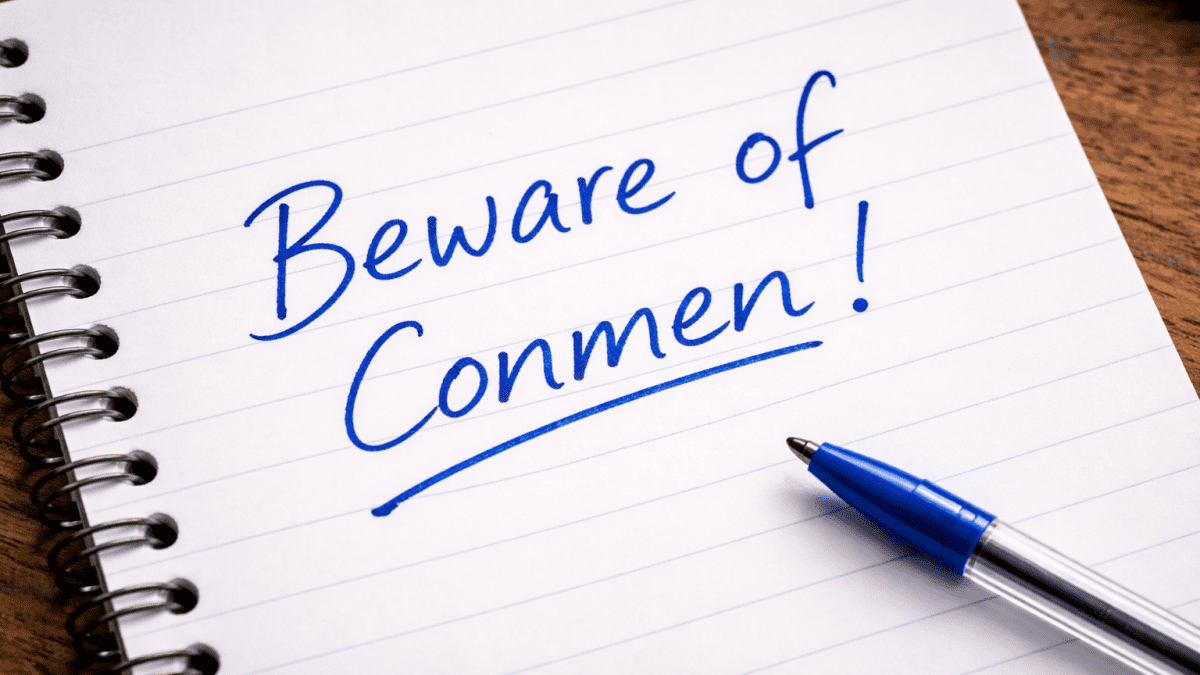 A handwritten warning reading “Beware of Conmen” in bold blue ink on a notebook, with a bic pen placed beside it. PHOTO/Photo generated by AI