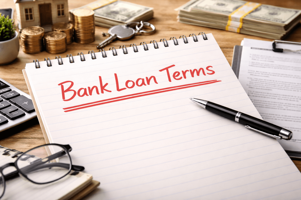 A lined notebook on a wooden desk displays “Bank Loan Terms” handwritten in bold red ink. PHOTO/Image generated by AI