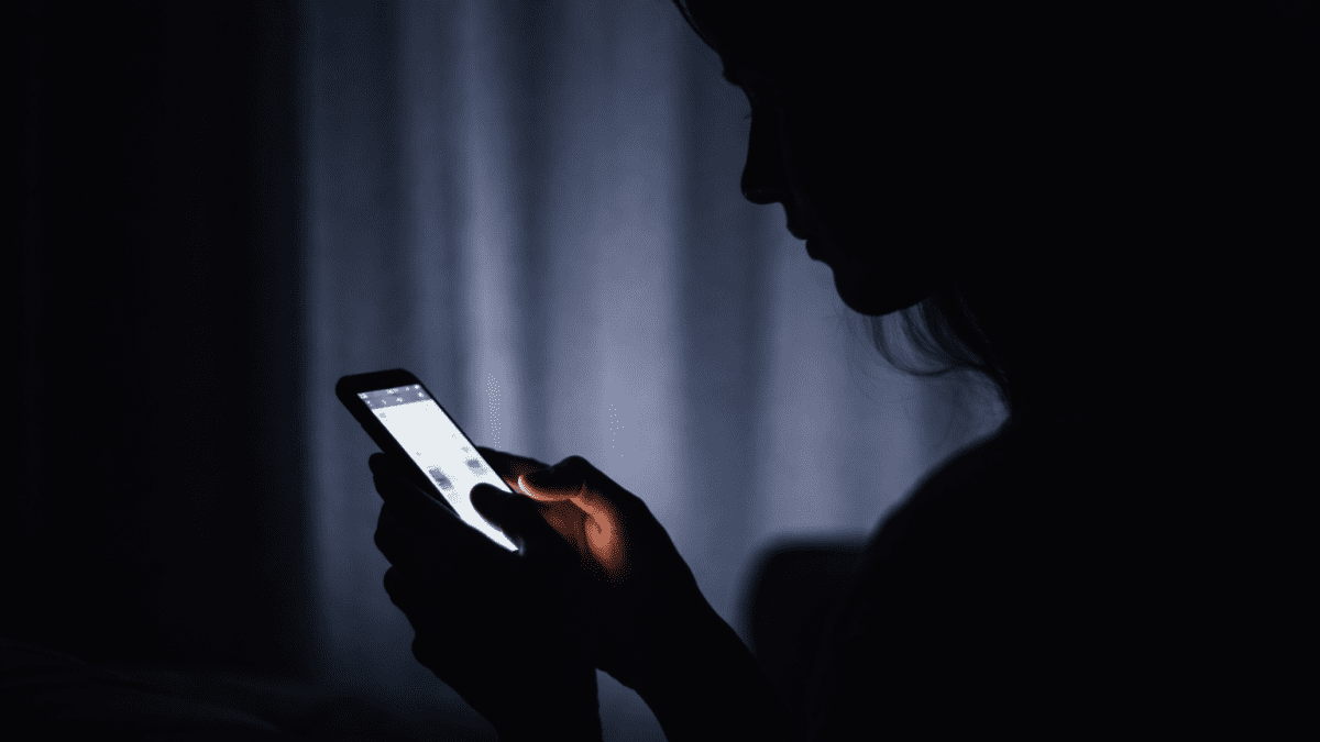 A sillhoette of someone using a smartphoen in darkness. PHOTO/Photo generated by AI