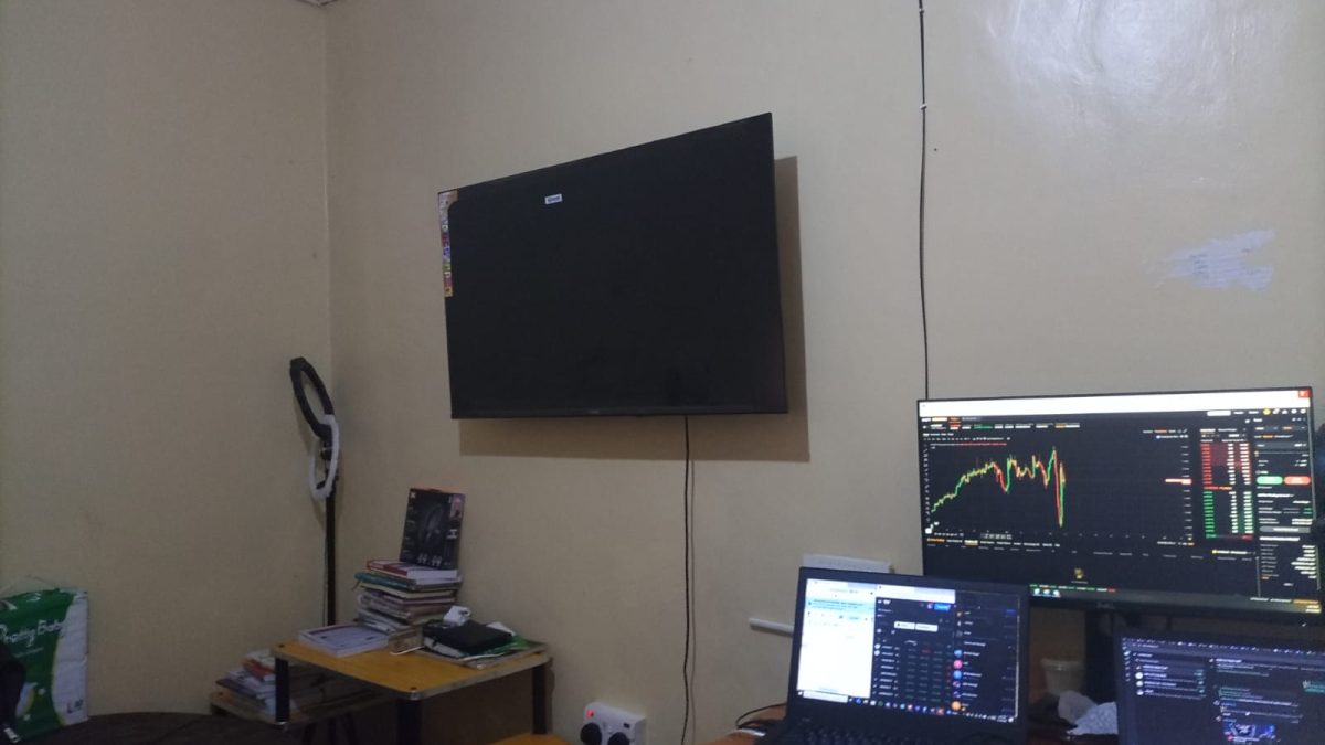 A wall-mounted television positioned above a home workstation with laptops and a monitor displaying charts, with visible wiring running down the wall to a power socket. PHOTO/David Nthua