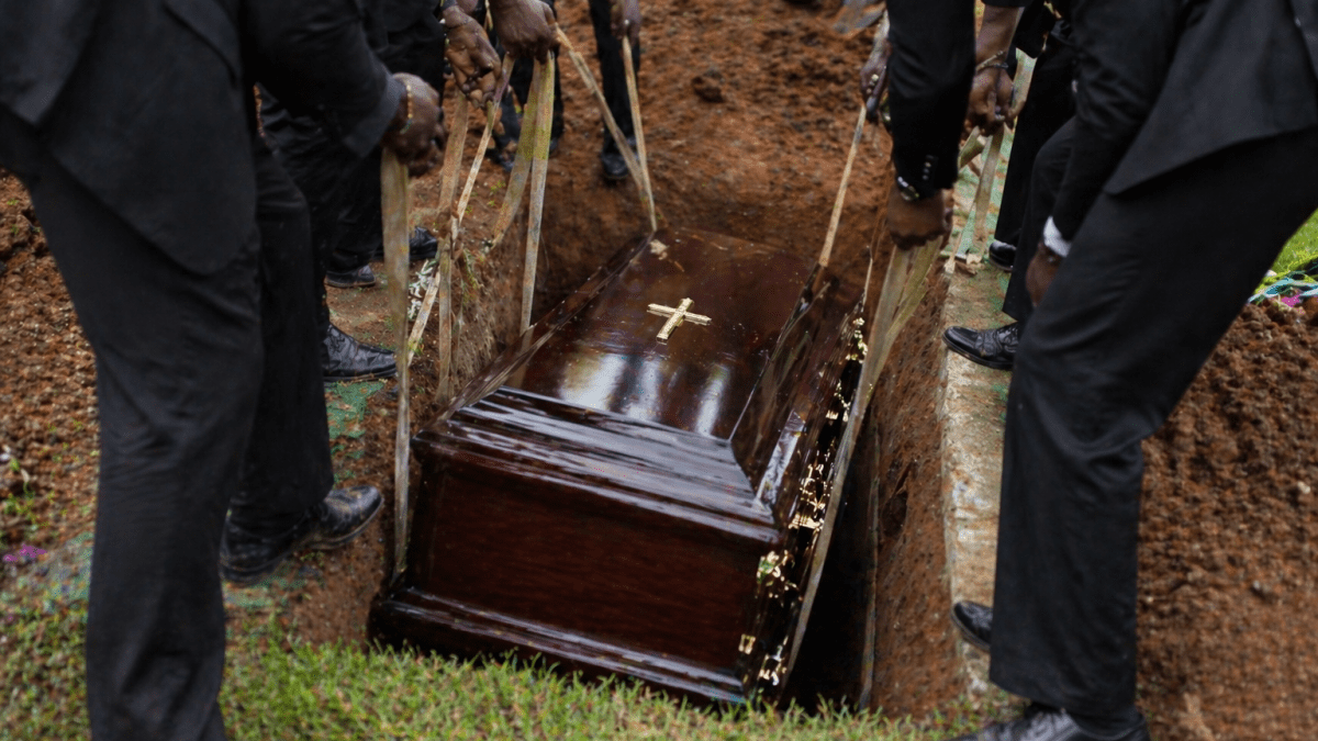 mourners in suits lowering a polished wooden casket into a grave at a burial site. PHOTO/Photo generated by AI