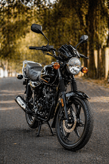 Black motorbike parked on a quiet road in portrait view, showing sleek bodywork, bright headlamp, strong tyres and a scenic tree-lined background. PHOTO/Photo generated by AI