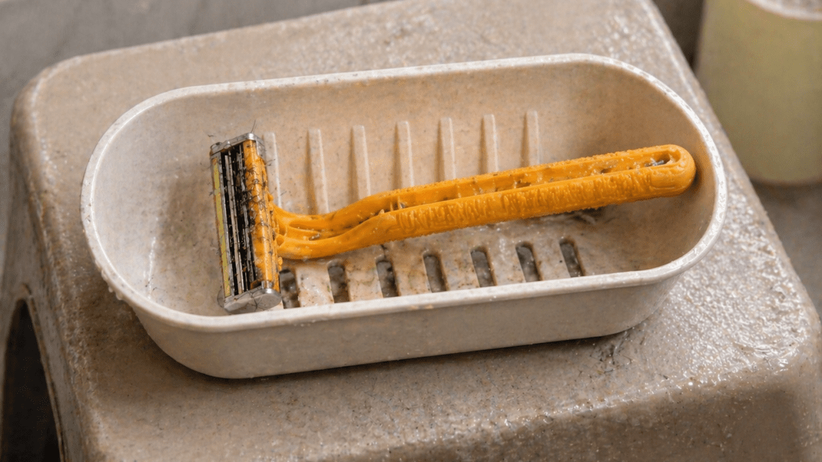 Disposable razor with hair trapped in the blades resting inside a plastic soap holder on a bathroom stool. PHOTO/Photo generated by AI