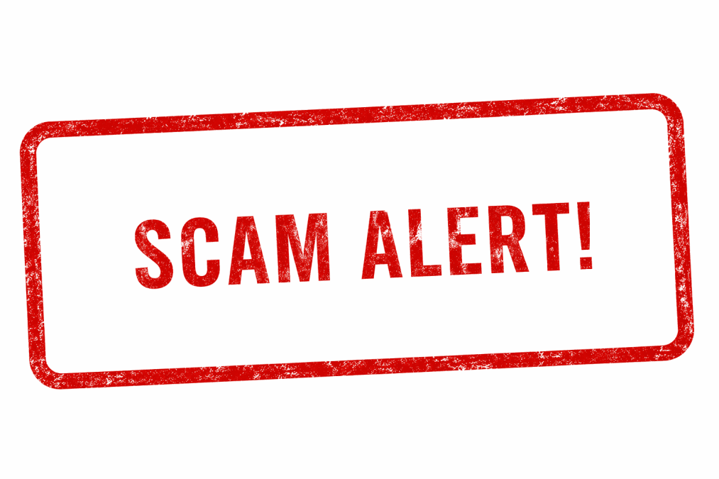 Red Scam Alert text inside a distressed warning stamp frame on a clean white background landscape banner. PHOTO/Photo generated by AI