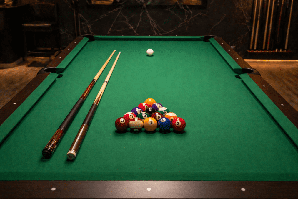 Close-up view of a green pool table with balls arranged in a triangle, two cue sticks placed beside them. PHOTO/Photo generated by AI