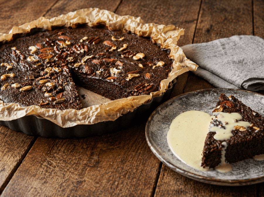 A rich chocolate cake topped with crunchy nuts, beautifully served with a smooth creamy drizzle for a warm and indulgent treat. 