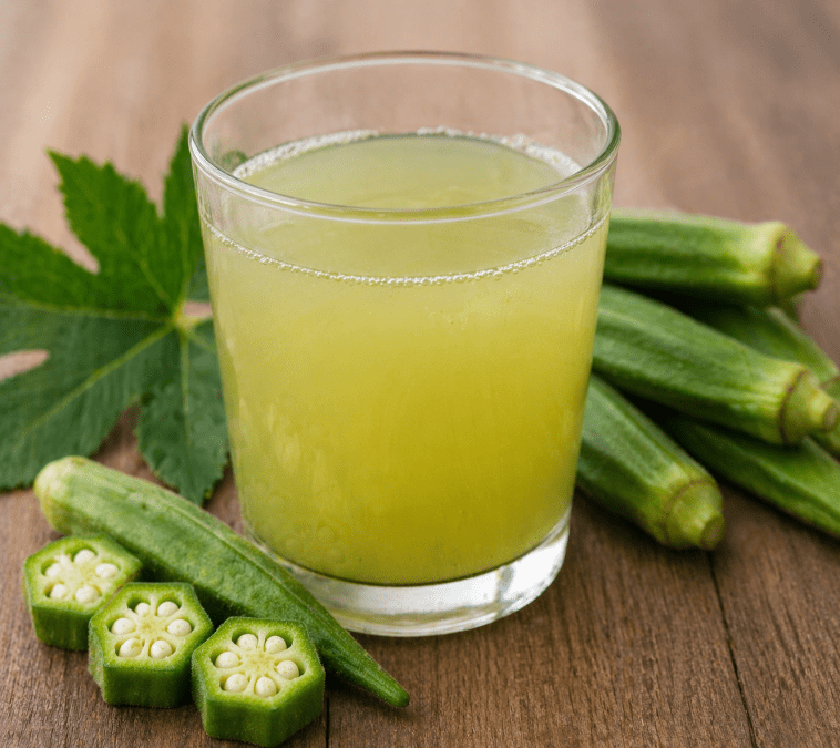 Glass of fresh okra juice on a wooden table surrounded by whole and sliced green okra pods in natural light. PHOTO/Photo generated by AI