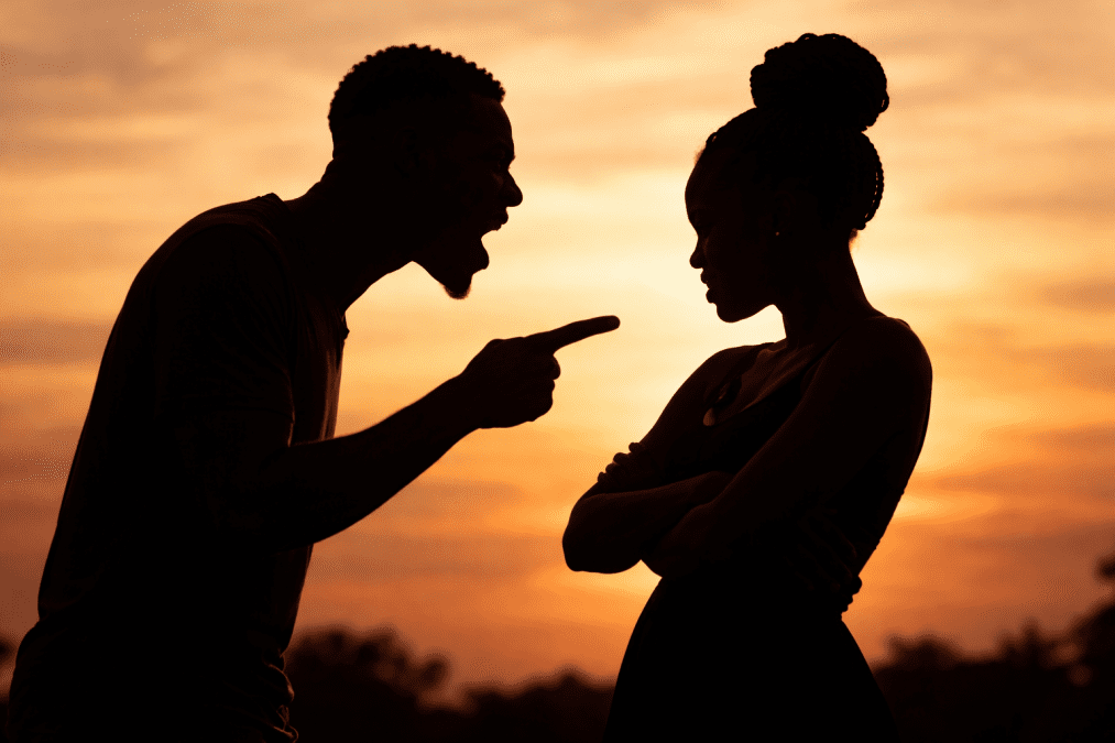Silhouette of couple in tense argument as man talks at his partner.
