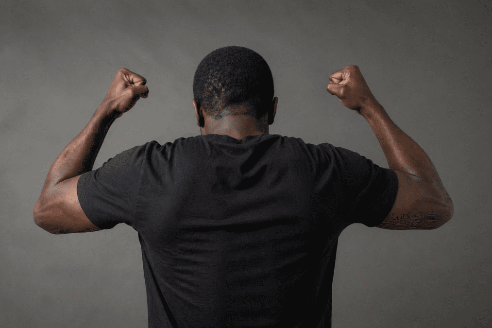 man seen from behind with raised clenched fists in an angry pose against a plain dark background. PHOTO/Photo generated by AI