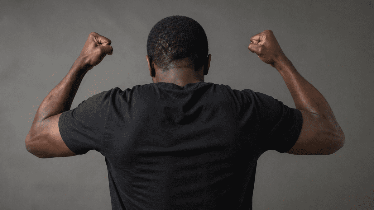 man seen from behind with raised clenched fists in an angry pose against a plain dark background. PHOTO/Photo generated by AI