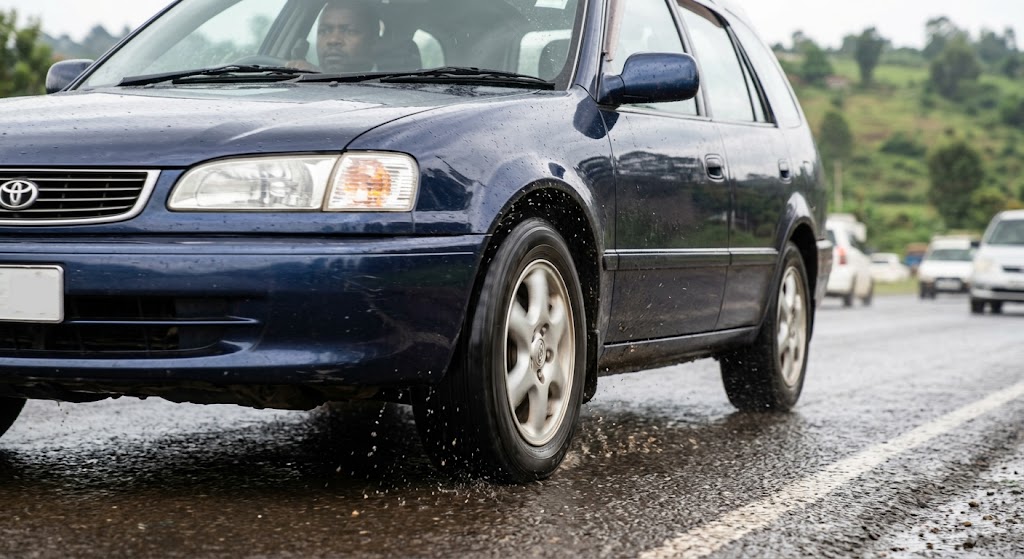 A car performs a hard, controlled stop on wet tarmac, with visible spray confirming the ABS is active.