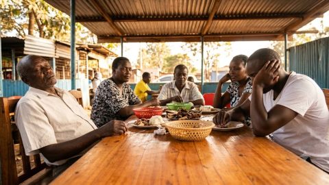 A family relaxes together around an outdoor table after sharing a large weekend meal.