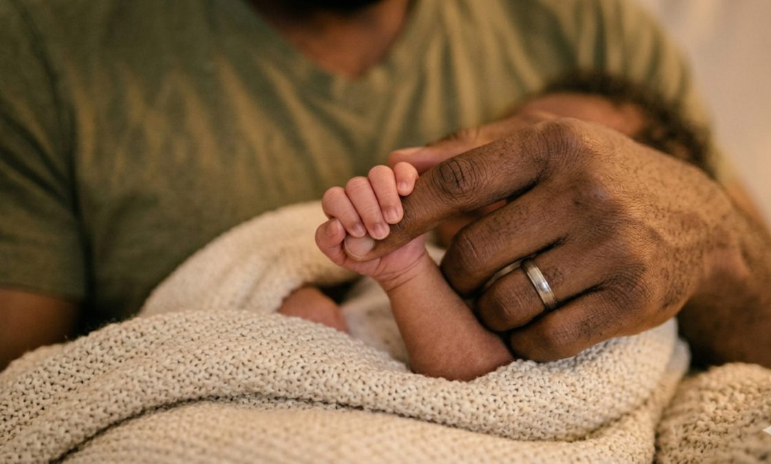 A newborn holding a man's index finger.