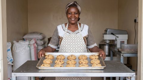 A smiling baker holding a large tray of uniform, perfectly baked biscuits.
