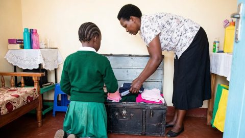 A parent helps a child pack a metal trunk for boarding school departure.