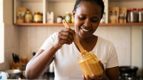 A woman stirs a fresh, smooth jar of groundnut butter in her kitchen.