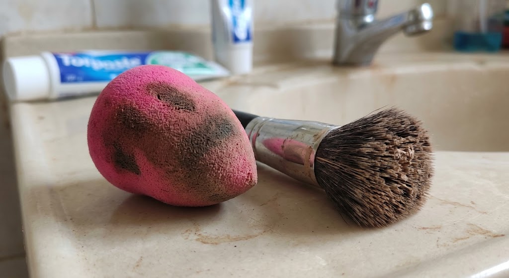 Significant foundation buildup and deep stains on a well-used makeup sponge and brush.