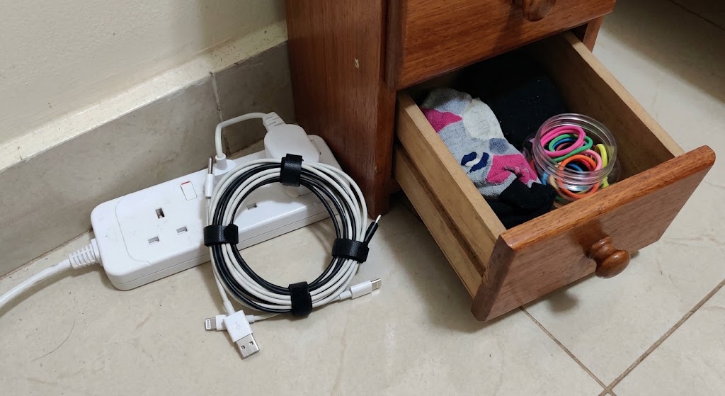 An extension lead is shown with all phone charger cables neatly bundled and organised using simple cable ties, preventing chewing hazards.