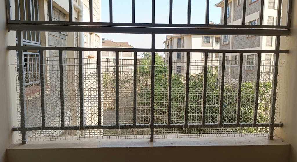 A durable plastic mesh is neatly fitted to the lower half of an apartment balcony railing to create a safety barrier.