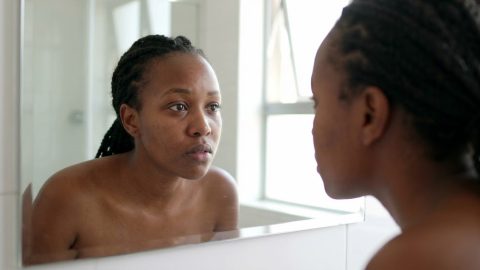 A woman examines her puffy morning face in a bathroom mirror.