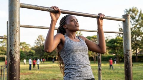 A young woman focuses on pulling herself up at an outdoor community fitness bar in a park.